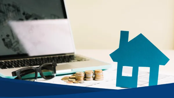 Mesa de trabajo con una computadora portátil, monedas apiladas y una figura azul en forma de casa, elementos que evocan el cálculo para gestionar un Credito Infonavit.